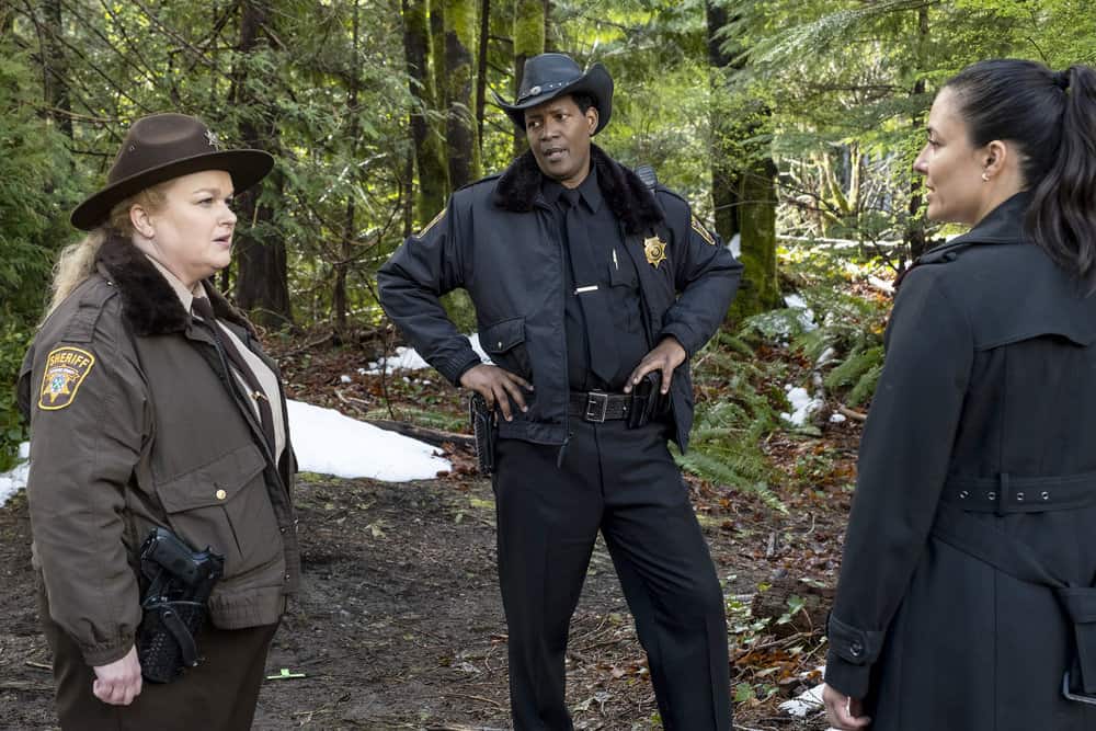 Three law enforcement officers engaged in a discussion in a wooded area.