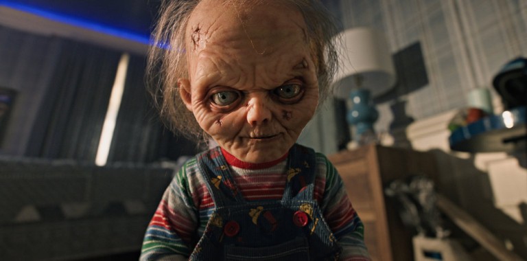 An animatronic doll with scars and intense eyes standing indoors.