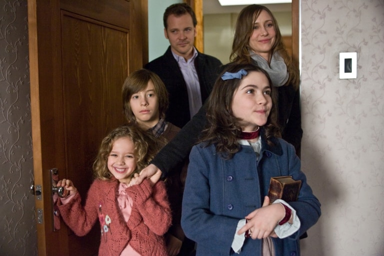 ‘Orphan’ (2009) Collector’s Edition Blu-Ray Review – A Go-For-Broke Creepy Kid Horror Favorite A family with two adults and three children standing at a doorway, looking towards something outside of the frame with expressions of anticipation or curiosity.
