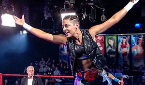 ‘Out In The Ring’ Blu-Ray Review – Enlightening Doc Explores Queer Representation In Wrestling A professional wrestler celebrating in the ring with a championship belt, arms raised, in front of a cheering crowd and a focused referee in the background.