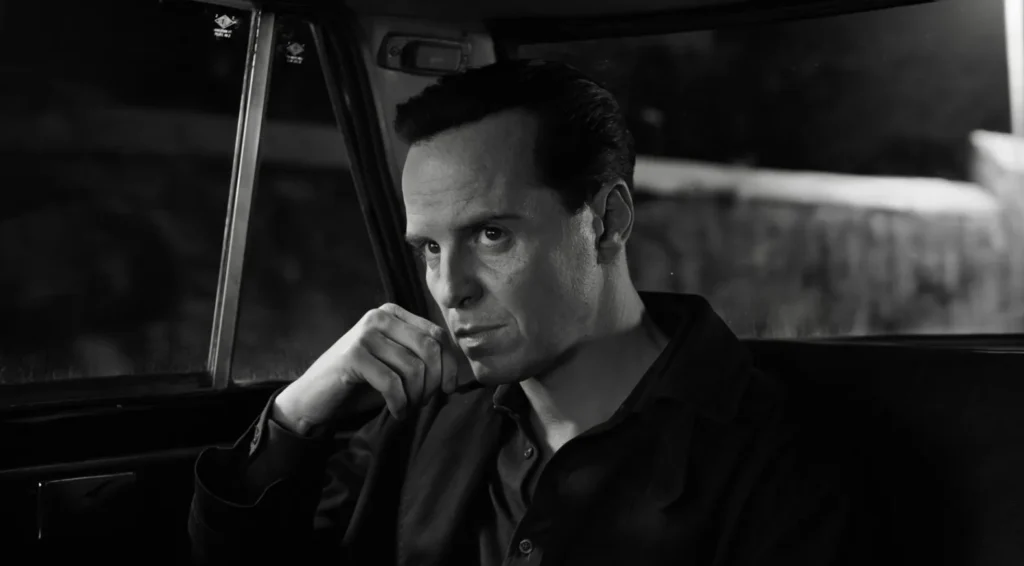 A man in a dark shirt, sitting thoughtfully in the backseat of a car at night, resting his chin on his hand.