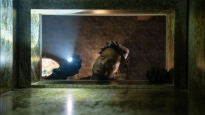 Man peering through a framed opening with a flashlight.