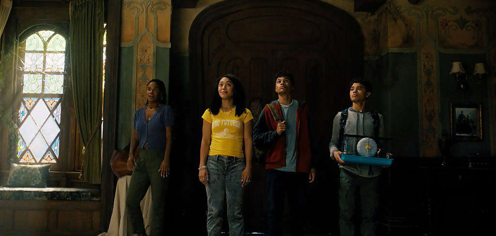 Four teenagers stand in awe inside a dimly lit, ornate room, looking towards a light source by the window.