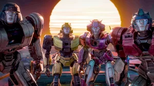 Four transformers, in various shades of blue and pink, stand together with a sunset in the background.