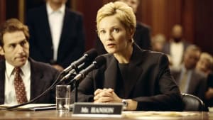 ‘The Contender’ (2000) Blu-Ray Review – Presidential Thriller Delivers With An All-Star Cast A woman with short blonde hair, dressed in a dark suit, speaks into microphones at a hearing, with a man seated next to her. a sign reads "mr. bannon" in front of them.