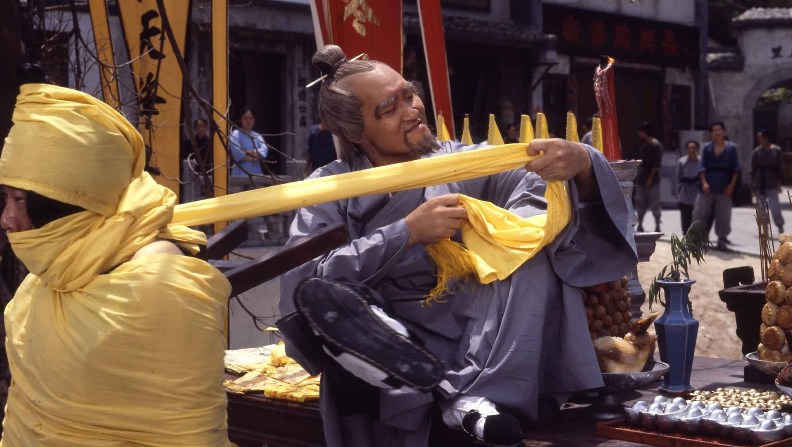 Man in traditional chinese attire playing a stringed instrument at a bustling market, with food vendors and flags in the background.