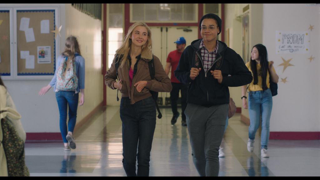 Two students walking down a school hallway, smiling and carrying backpacks.