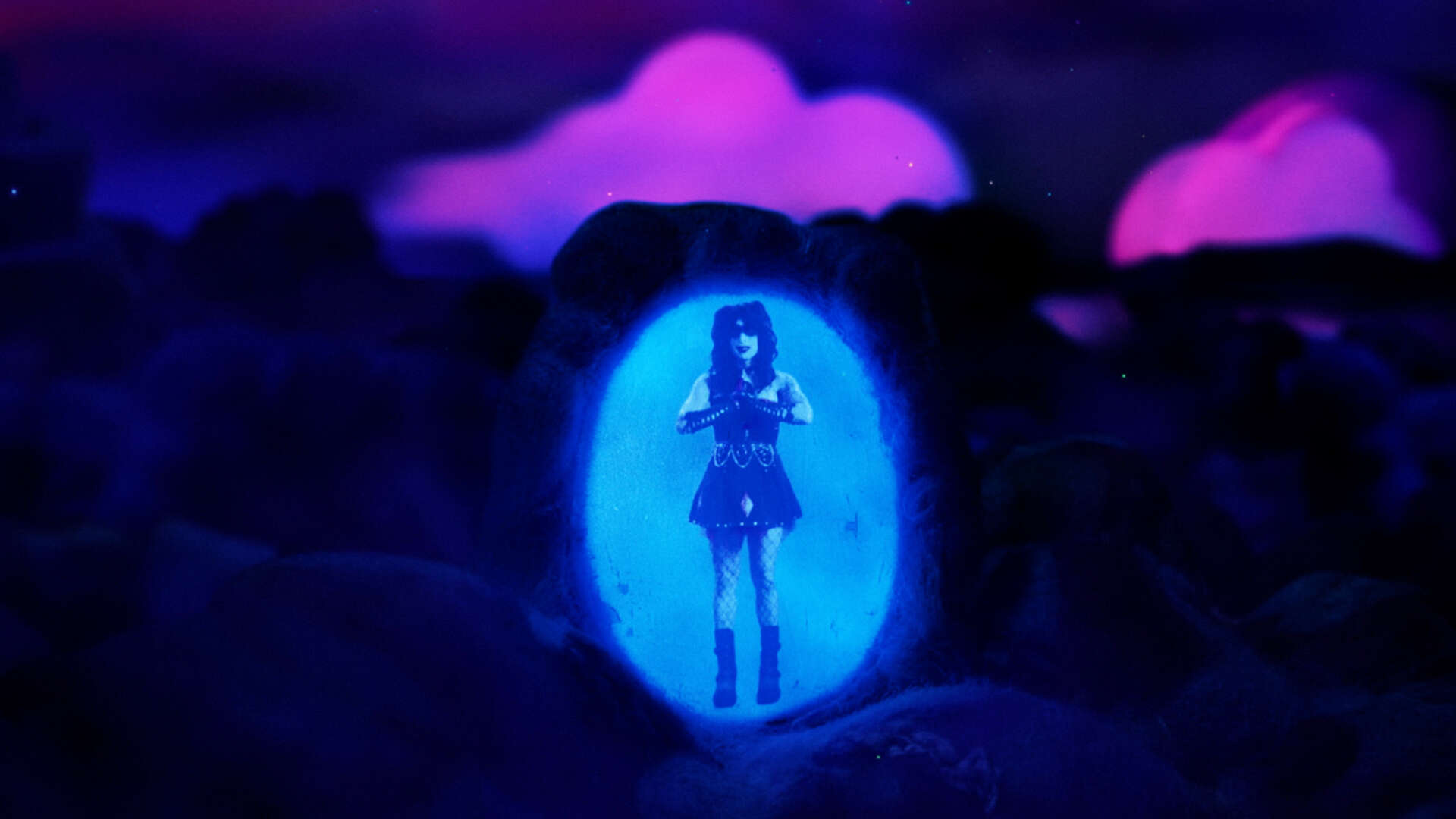 A holographic projection of a woman standing in a rocky environment under a purple sky with glowing clouds.