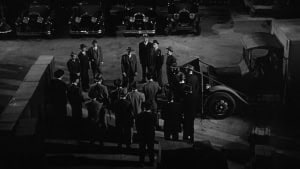‘The Scarface Mob’ Arrow Video Blu-Ray Review – An Engaging Dramatization Of The Al Capone Saga A group of men in long coats standing around in a dimly lit parking lot at night, surrounded by vintage cars.