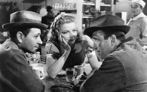 Three people engaged in conversation at a diner table, with one woman and two men wearing hats.