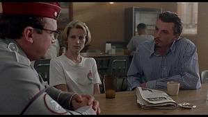 ‘Touch’ (1997) Blu-Ray Review – Paul Schrader’s Darkly Funny And Compelling Satire A tense conversation between three people in a diner; a woman and two men, one in a uniform, sitting at a table with a newspaper and drinks.
