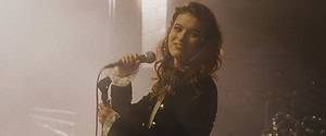 A woman singing on stage with a microphone, highlighted by soft stage lighting with a smoky background.