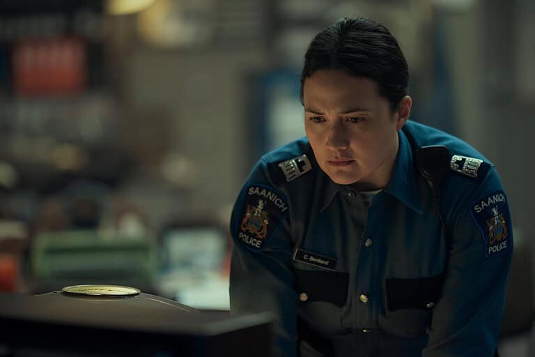 A police officer wearing a badge marked "sandwich police" looks intently at a computer screen in a dimly lit office.