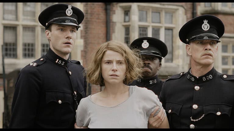 A woman in a white dress looks distressed while being escorted by four police officers in uniforms outside a historical building.