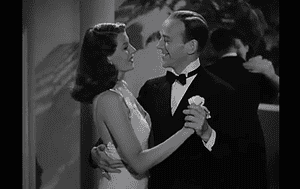 ‘You’ll Never Get Rich’ Blu-Ray Review – A Cinematic Delight From Rita Hayworth And Fred Astaire A man in a tuxedo and a woman in a white gown are dancing and smiling at each other in a black-and-white movie scene.