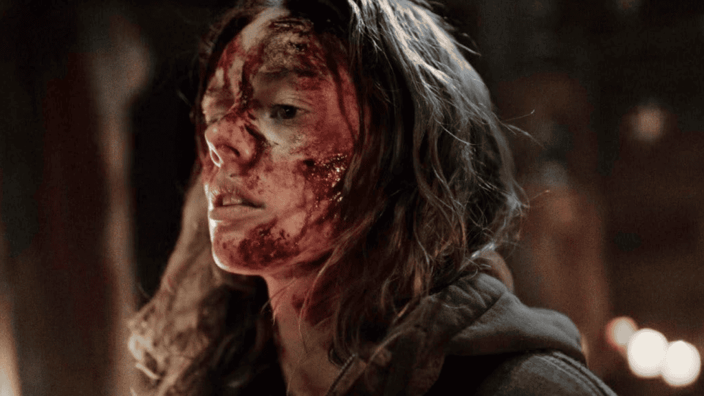 A woman with disheveled hair appears distressed and bloodied, her face marked with injuries, standing in a dimly lit room.