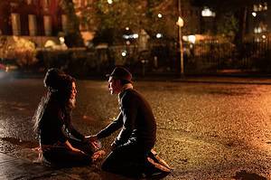 ‘Back To Black’ Blu-Ray Review – A Misguided Look A The Life Of Amy Winehouse A couple sits on a wet street at night, holding hands and facing each other with a softly lit park fence in the background.