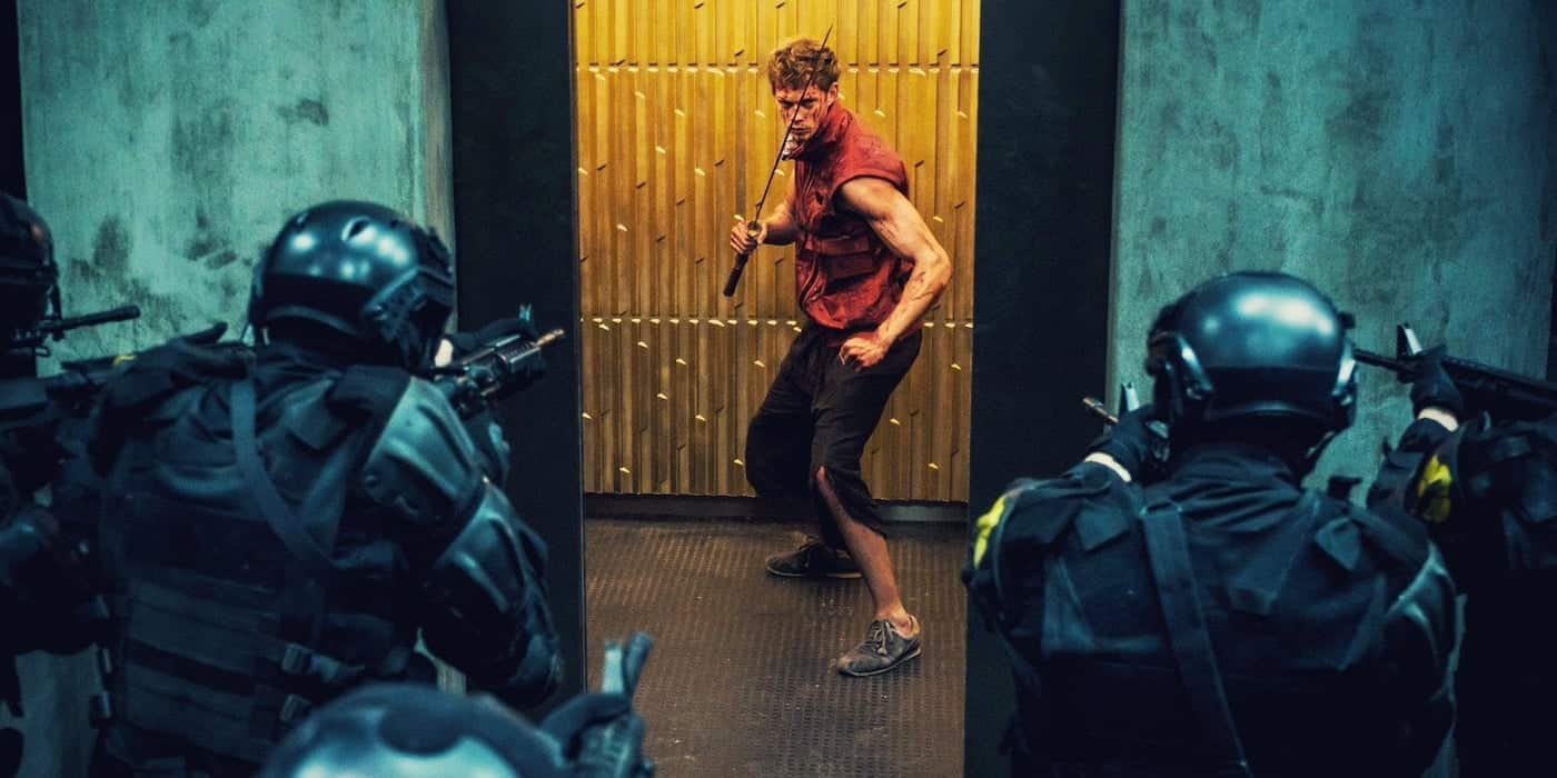 A man with a battered appearance and a metal rod faces off against several armored police officers in a dimly lit corridor.