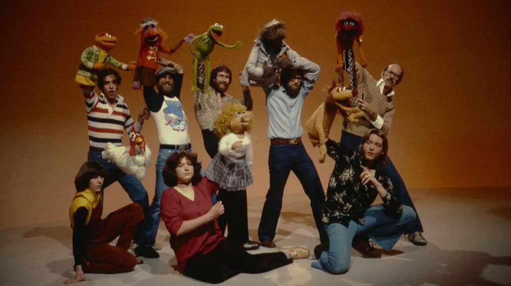 Jim henson and his team posing with muppet characters including kermit and miss piggy, in a studio setting.