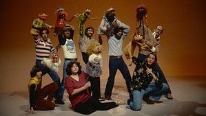 Disney+ And Ron Howard Debuts Compelling Jim Henson Documentary Trailer Jim henson and his team posing with muppet characters including kermit and miss piggy, in a studio setting.