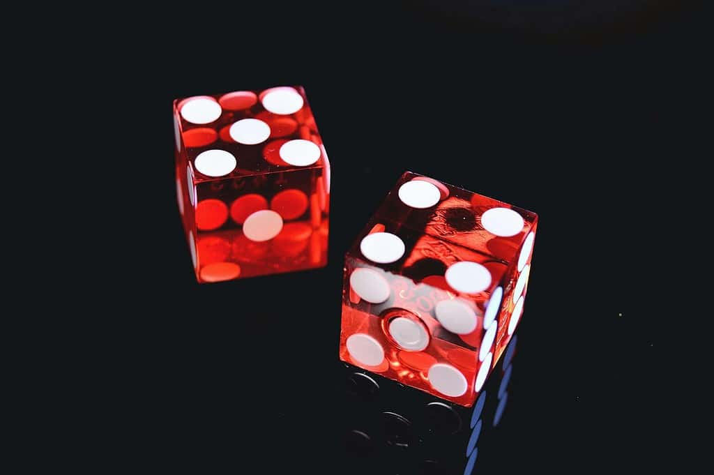 Two red dice with white dots on a reflective black surface, showing a four and a one.