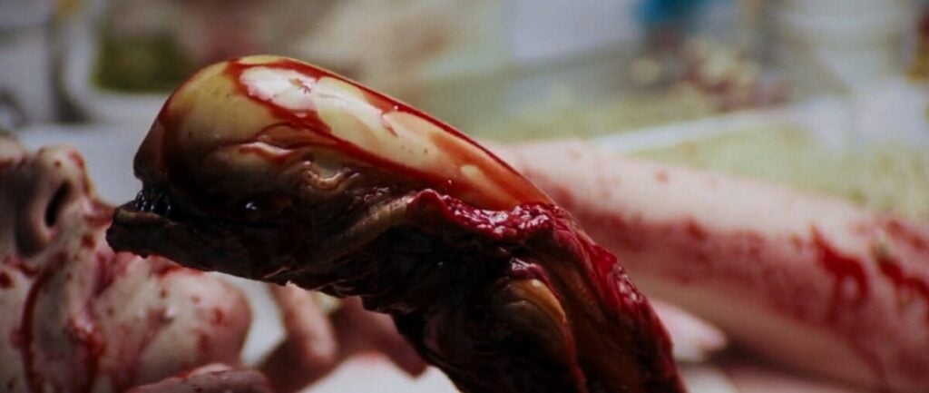 Close-up of a grotesque alien creature coated in blood, emerging from a person's chest in a sci-fi horror scene.