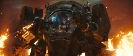 Person piloting a large armored mech unit, surrounded by flames and debris in a fiery environment.