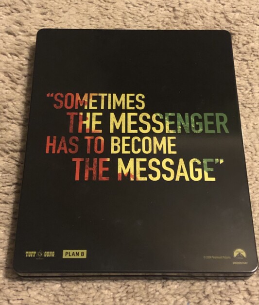 A black box with colorful text reading, "Sometimes the messenger has to become the message," placed on a light-colored carpet. Logos for Tuff Gong, Plan B, and Paramount Pictures are visible at the bottom.