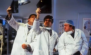 Three doctors in white coats examining x-ray films in a hospital room.