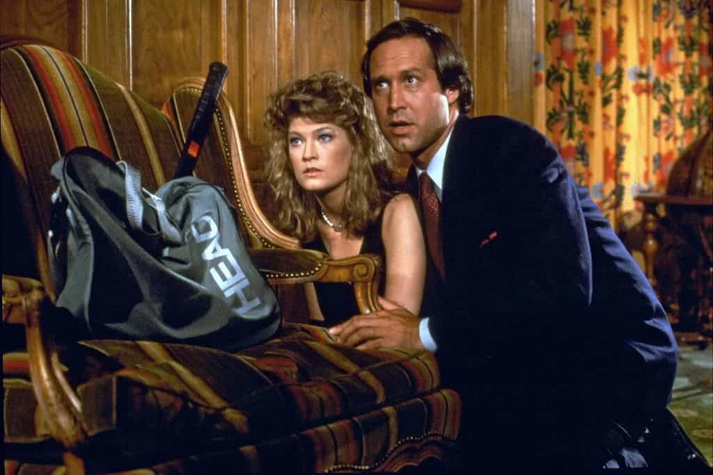 A man and a woman hiding behind a couch in a vintage-styled room, looking anxious and cautious.