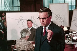‘JFK’ 4K UHD Blu-Ray Review – A Conspiracy Epic For The Ages A man in a suit and glasses gestures emphatically in a courtroom setting, with sketches and observers in the background.