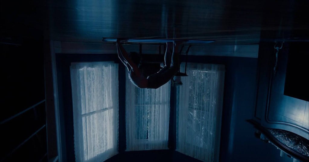 Spider-man hangs upside down in a dark room, illuminated by moonlight streaming through window blinds.