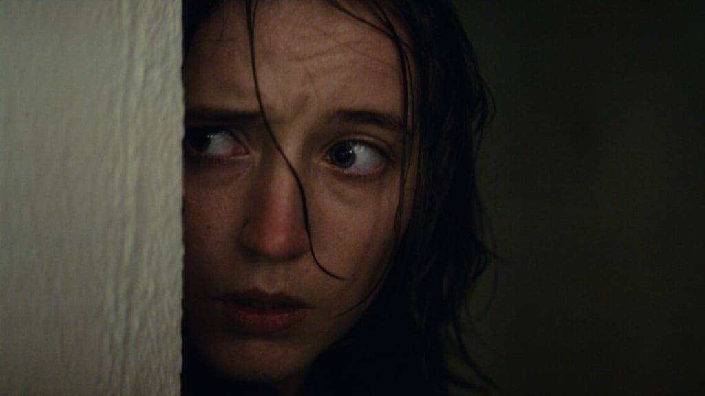 A worried woman with wet hair peeking from behind a wall, her face partially visible, looking to her right with wide, fearful eyes.