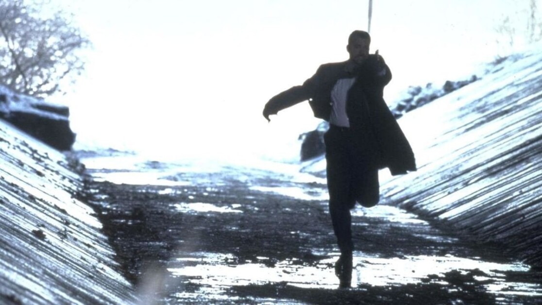 A person in a suit runs on a snowy, sloped path with their arm extended forward.
