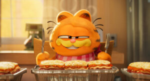 Animated orange cat with black stripes and a smug expression sits at a table with trays of lasagna, holding a fork and knife.