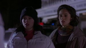 ‘Phantoms’ 4K UHD Blu-Ray Review – A Tonally Imbalanced But Entertaining Horror Outing Two women wearing winter coats look intently at someone off-camera, standing outside at night with blurred lights in the background.