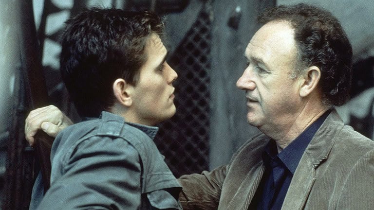 ‘Target’ (1985) Blu-Ray Review – A Talented Cast Elevates This Spy Thriller Two men having a serious conversation; a younger man with an intense expression holds an older man by the collar against a metal grate background.