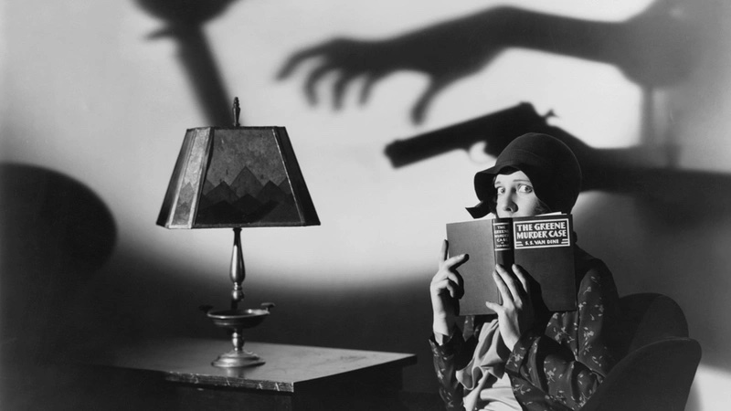 A woman reads "The Greene Murder Case" as alarming shadows of a hand and gun loom on the wall behind her, with a lamp on the table to her left.
