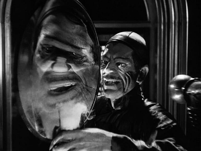 A person with a sinister expression looks at their distorted reflection in an oval mirror with curved edges, creating an eerie and macabre scene.
