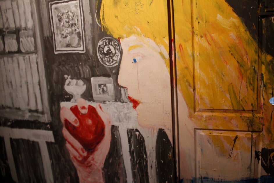 A mural depicting a stylized woman holding an apple, rendered in bold colors, with details including books and portraits in the background.