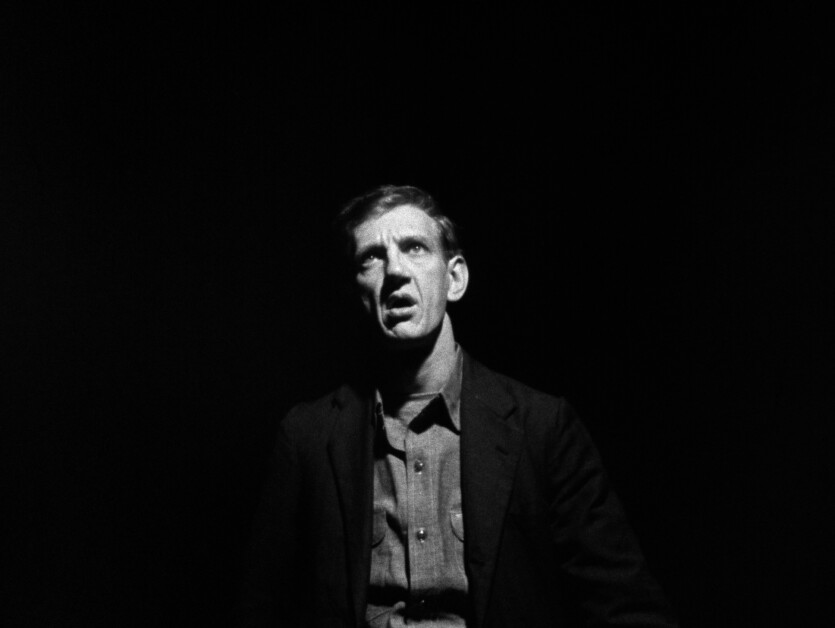 Black and white image of a distressed middle-aged man looking upward, illuminated against a dark background.