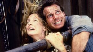 Two people cling to a metal beam with strained expressions, suggesting they are in a state of distress or facing extreme conditions.