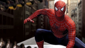 Spider-Man crouching on a metal surface in an urban setting, poised to leap, with a blurred city background.