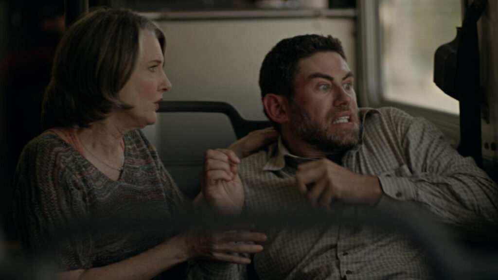 A woman and a man sit closely on public transportation, looking out of the window with anxious expressions. The man appears particularly tense, gripping the woman's arm.