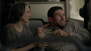 ‘We Go On’ Remastered Blu-Ray Review – The Search For An Afterlife Is A Fool’s Errand A woman and a man sit closely on public transportation, looking out of the window with anxious expressions. The man appears particularly tense, gripping the woman's arm.