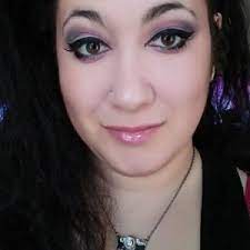 A person with long dark hair wearing makeup and a necklace, looking at the camera with a slight smile.