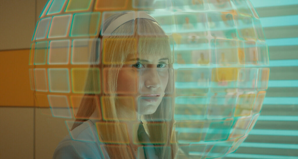 A person wearing a headpiece is standing behind a transparent spherical grid with colored squares.