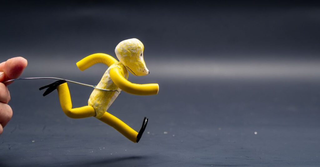 A hand manipulates a yellow, flexible toy figure in a running pose against a dark background.
