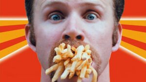 A person with wide eyes has a large amount of French fries in their mouth against an orange background with yellow rays.
