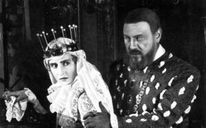 ‘Anna Boleyn’ (1920) Blu-Ray Review – Ernst Lubitsch Injects History With Life In Early Silent Effort Two actors in historical costumes perform a dramatic scene; the woman wears a crown and the man has a beard and royal attire.